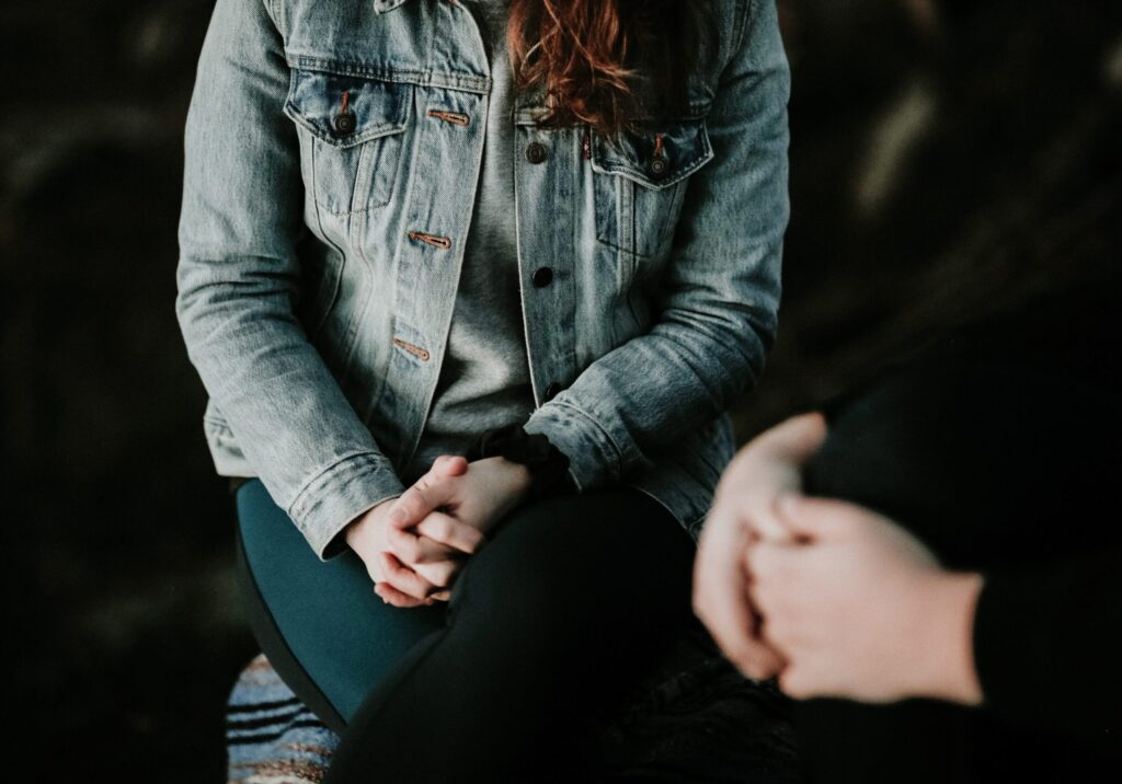 Two people sitting and talking, hands folded.